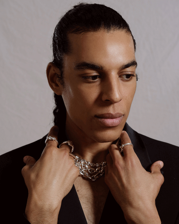 Portrait of man wearing silver CRZM necklaces and rings.