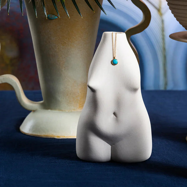 Minimalist Collection ceramics featuring a vase in the shape of woman, glazed planter and Mociun turqu, on navy tabletop.