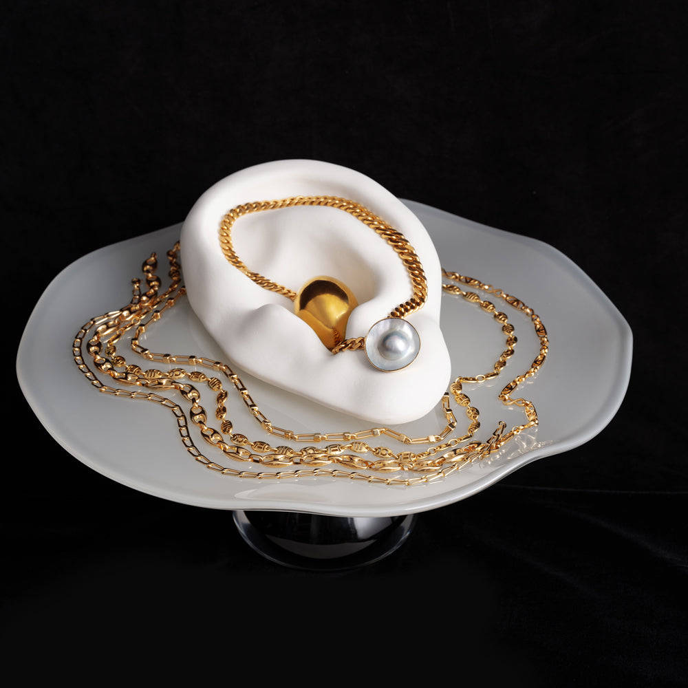 Photo of gold chains laid a Bon Bon Cake Stand, on a black background.