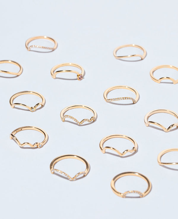 Group of Mociun Wedding Bands and Stacking Rings of varying styles and gemstones on light color surface.
