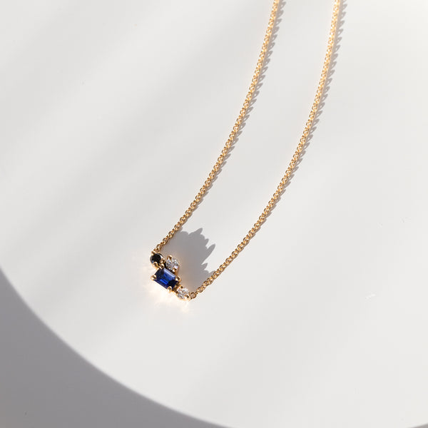 Gifts that Sparkle Collection gold chain necklace with a blue sa, on a white tabletop.