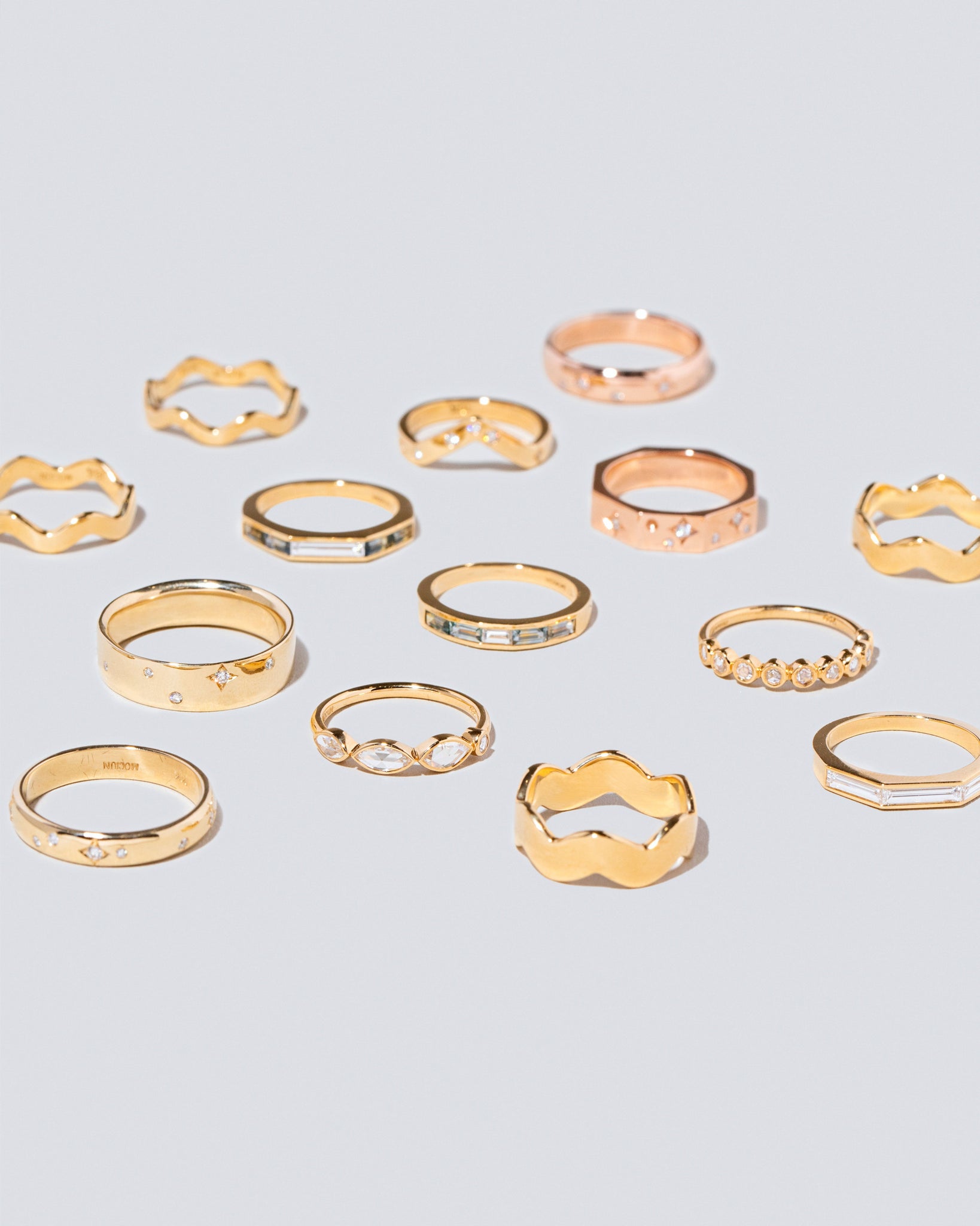 Group of Mociun Solid and Gemstone Wedding Bands and Stacking Rings of varying styles and gemstones on light color surface.