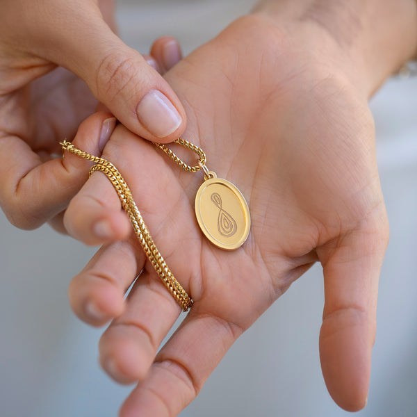 Mociun yellow gold Memento Pendant and yellow gold chain in hand.