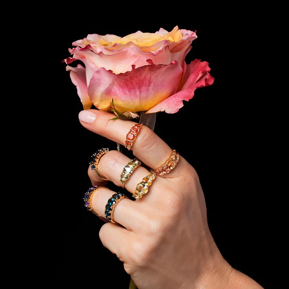 Model's hand wearing line cluster rings and holding a rose.