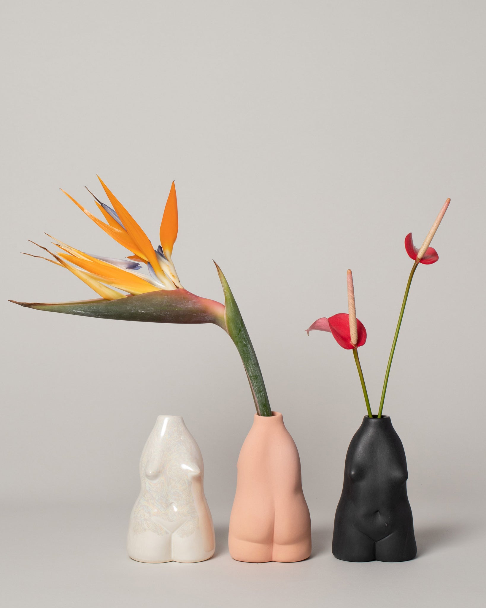 Rachel Saunders Collection Woman vases in white, peach and black  with orange and red florals, on a neutral-light background.
