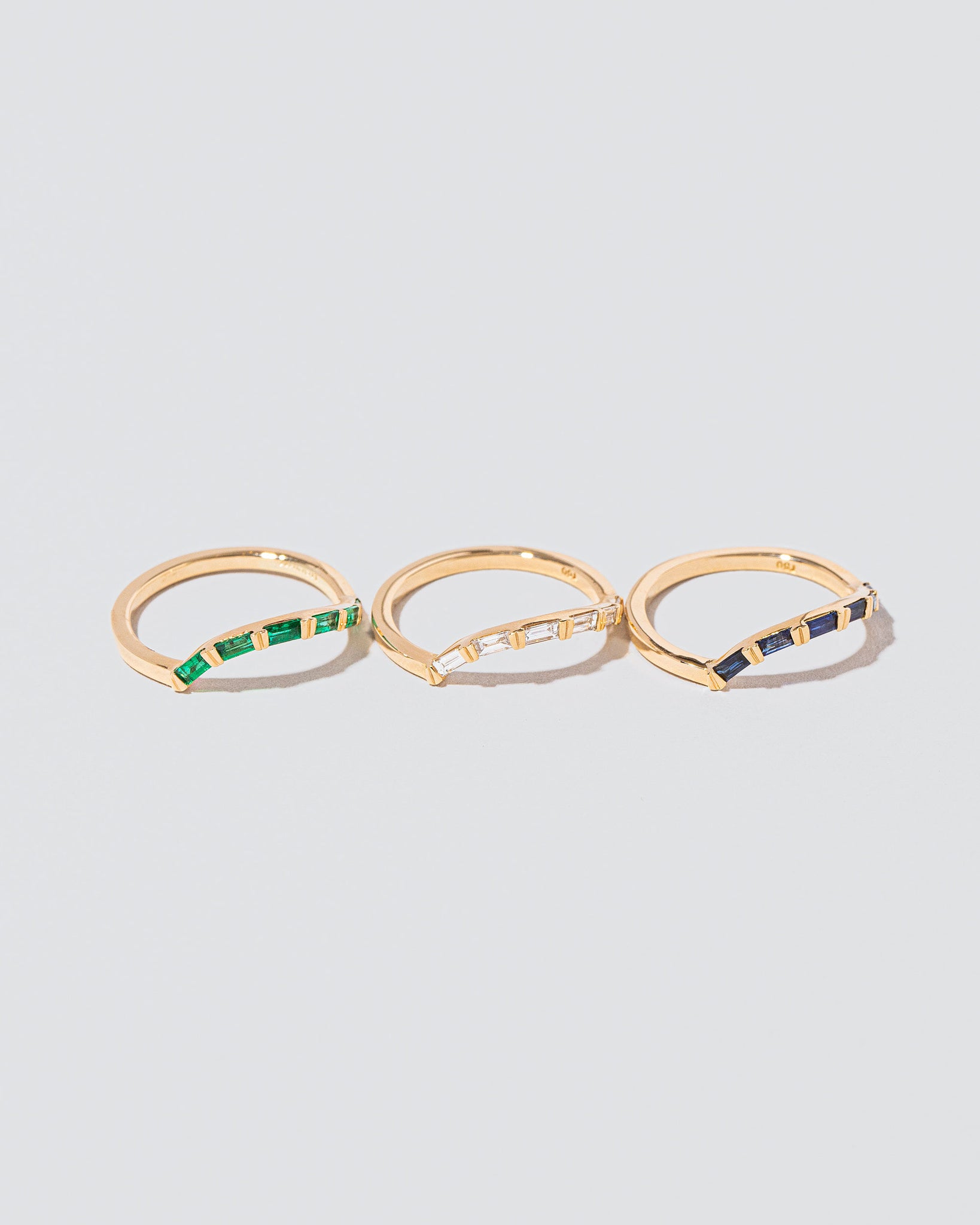 Group of Mociun Shape Collection Wedding Bands and Stacking Rings of varying styles and gemstones on light color surface.