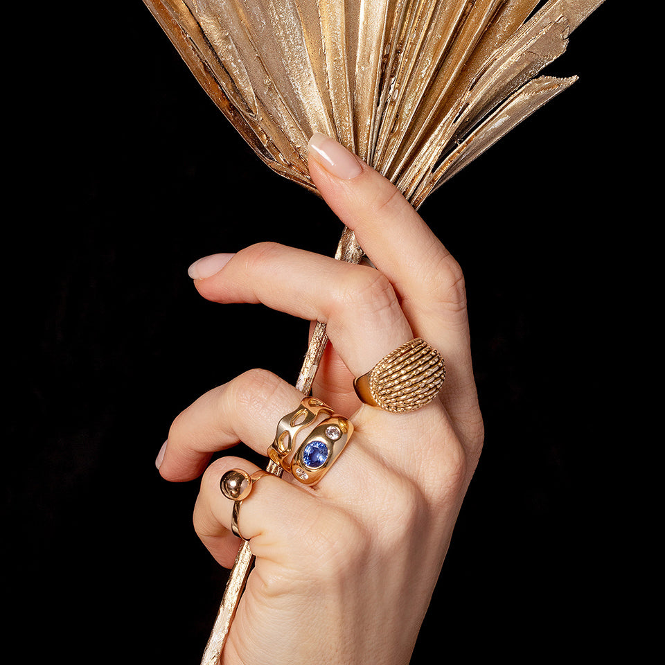 Anniversary Gifts Collection jewelry pieces shown on a model's hand, holding a gold stem, in front of a dark background.