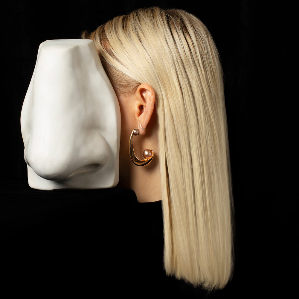 Photo of a floating head wearing a gold hoop earring on a black background. 