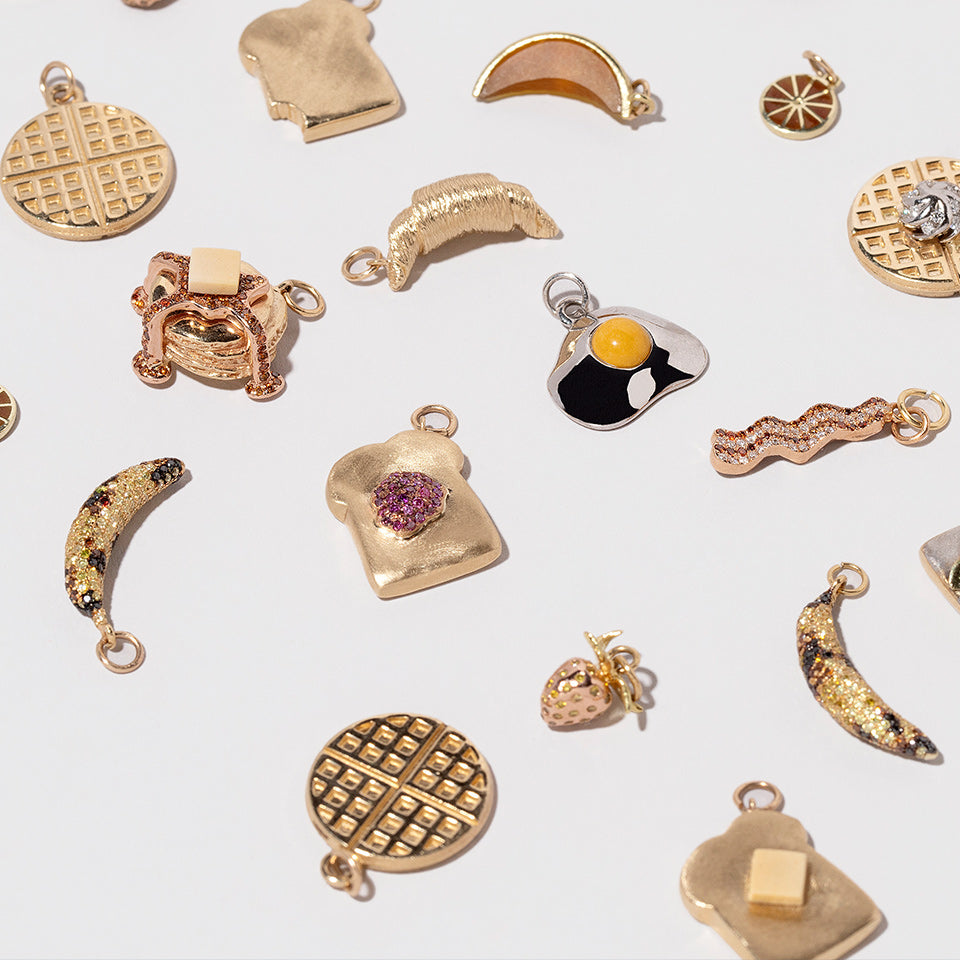 Morning People Collection yellow gold charms with enamel details, on a white tabletop.