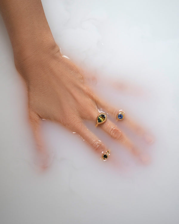 Styled image of model's hand in milky water, wearing three different Align Rings with bicolor and blue sapphires.