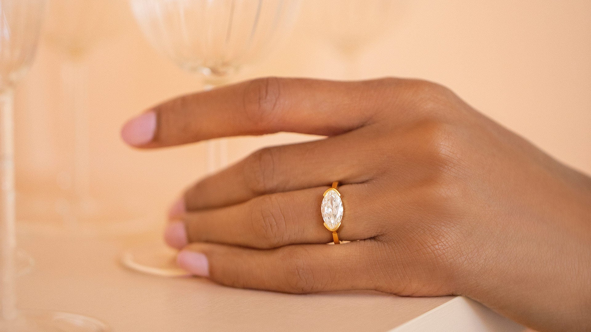 Model's hand wearing the Vivacity Ring on peach color background