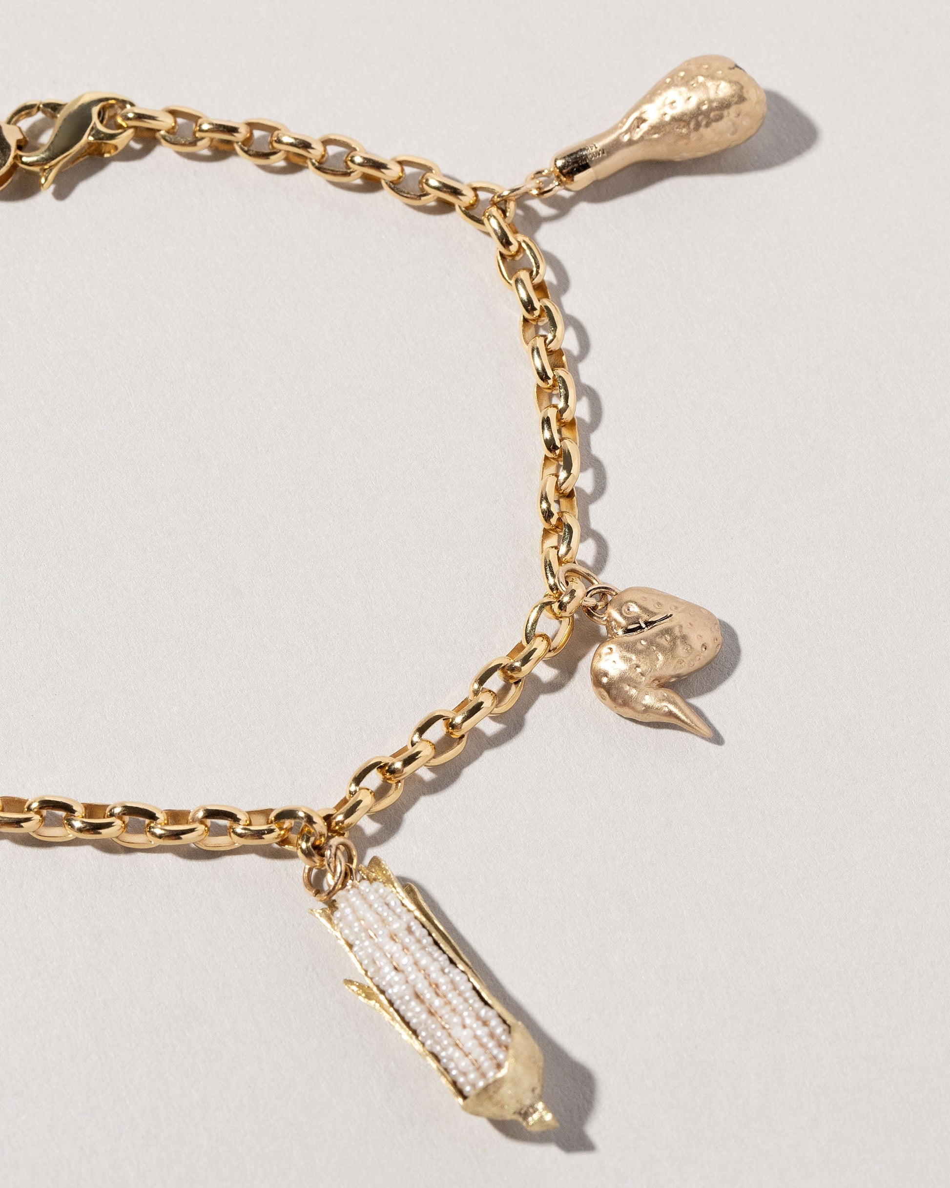 Closeup details of the Chicken Drumstick Charm, Chicken Wing Charm and Corn on the Cob Charm with Gold Endless Clasp Bracelets on light color background.