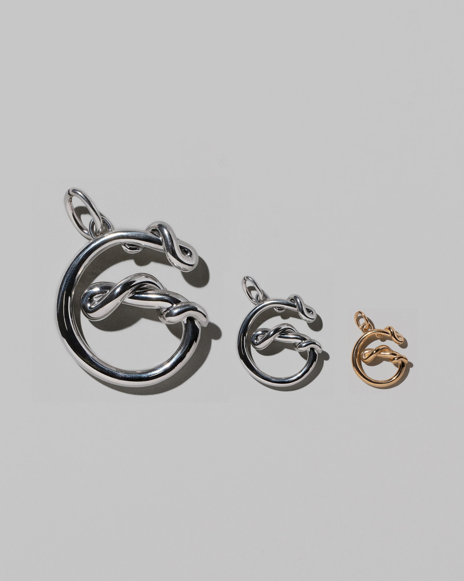 CRZM Large Sterling Silver, Medium Sterling Silver & Mini Letter G Charms set in solid gold on light color background.