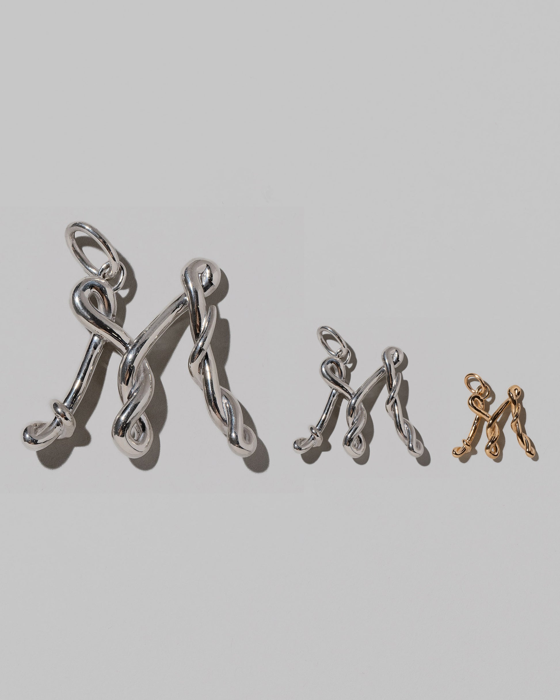 CRZM Large Sterling Silver, Medium Sterling Silver & Mini Letter M Charms set in solid gold on light color background.