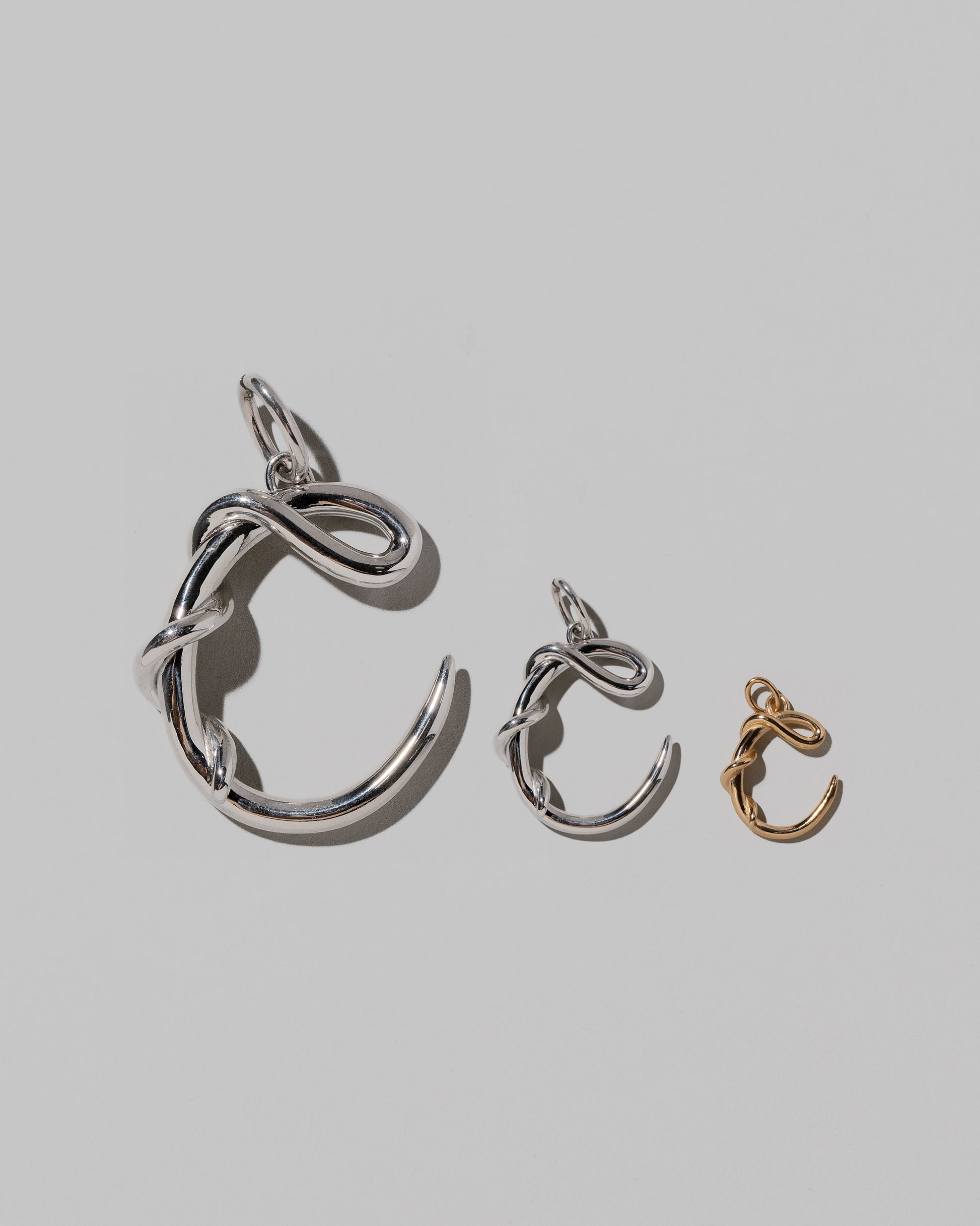 CRZM Large Sterling Silver, Medium Sterling Silver & Mini Letter C Charms set in solid gold on light color background.