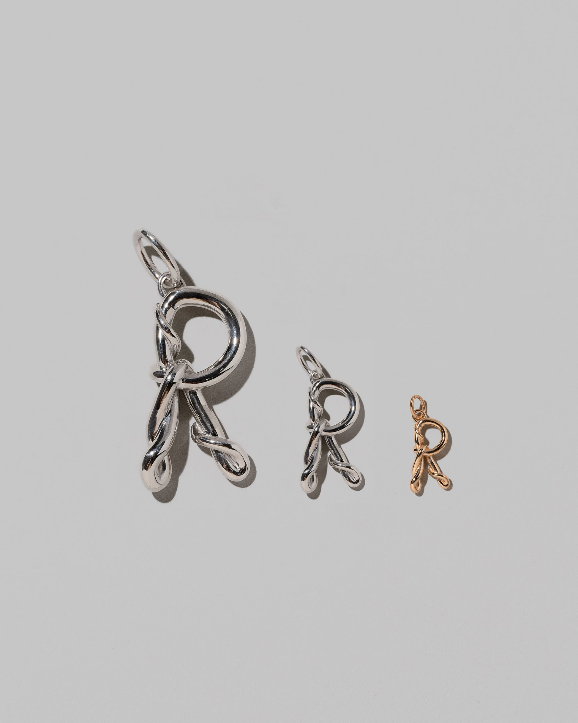 CRZM Large Sterling Silver, Medium Sterling Silver & Mini Letter R Charms set in solid gold on light color background.