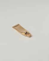 View from the side of the Pearce Objects Cast Bronze Travel-Sized Toothpaste Tube on light color background.