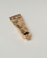 Closeup details of the Pearce Objects Cast Bronze Paint Tube on light color background.