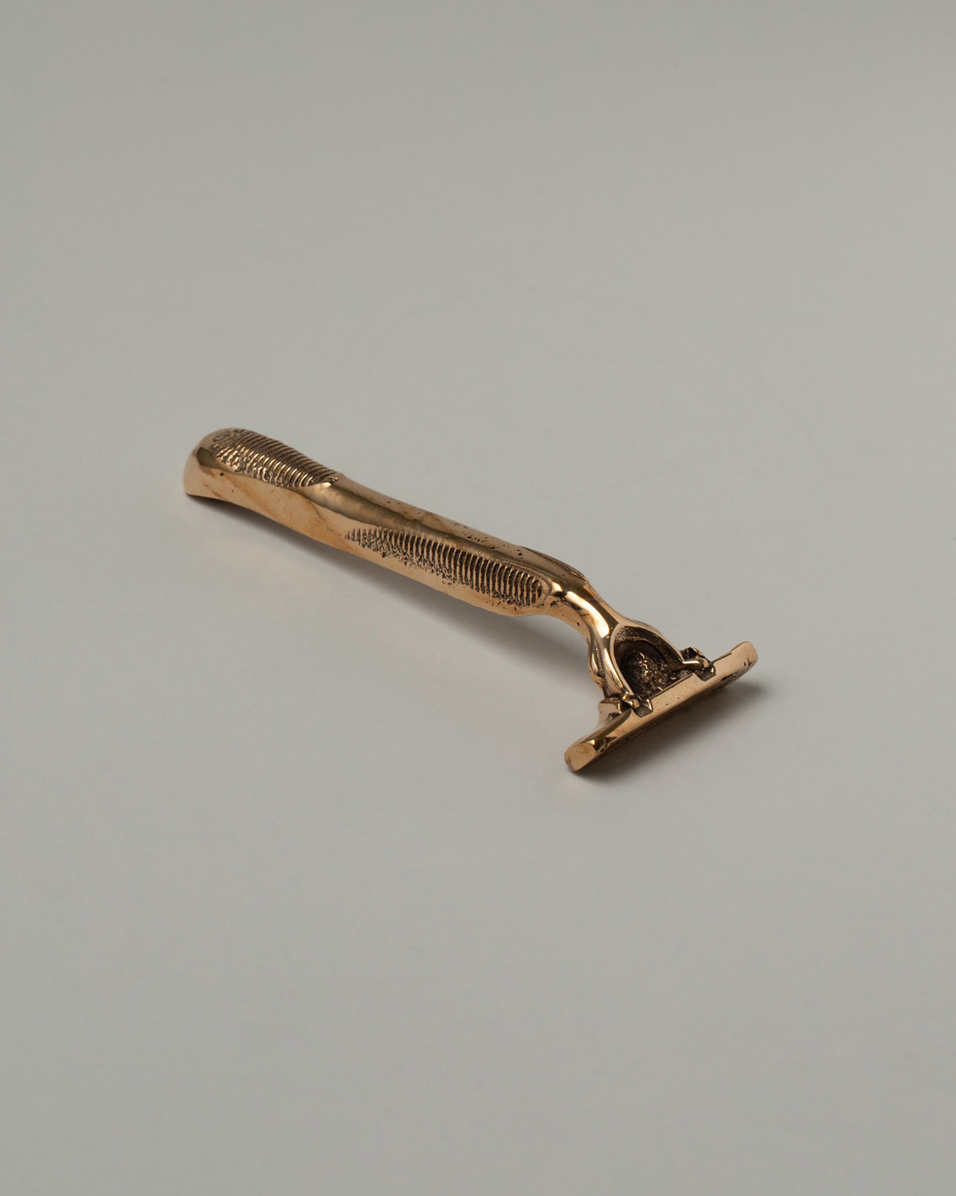 View from the side of the Pearce Objects Cast Bronze Razor on light color background.
