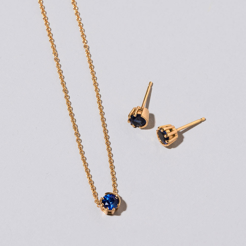 product_details::Closeup details of the Sapphire Sun & Moon Necklace & Studs Set on light color background.