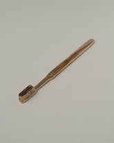 View from the side of the Pearce Objects Cast Bronze Toothbrush on light color background.