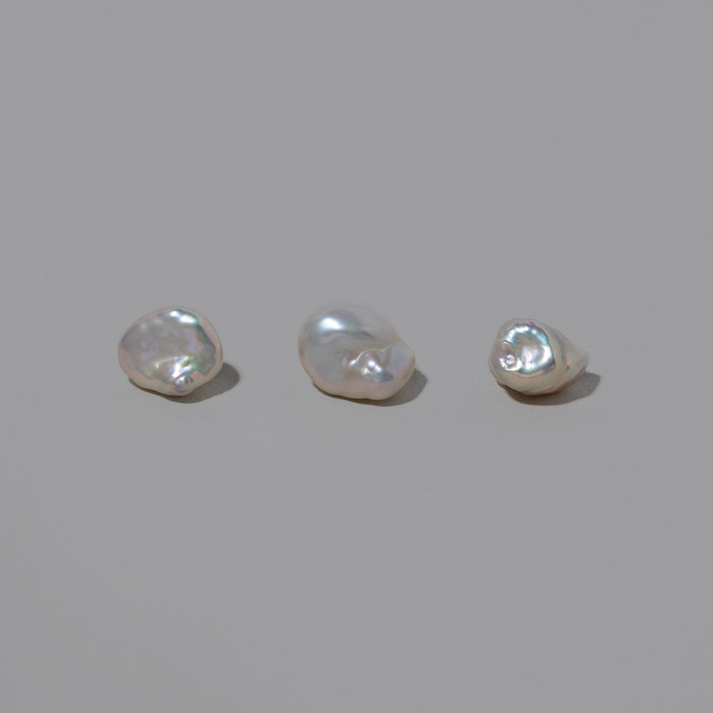 product_details::Closeup details of a group of Natural Lagniappe Pearl Stud Earring Singles on light color background.