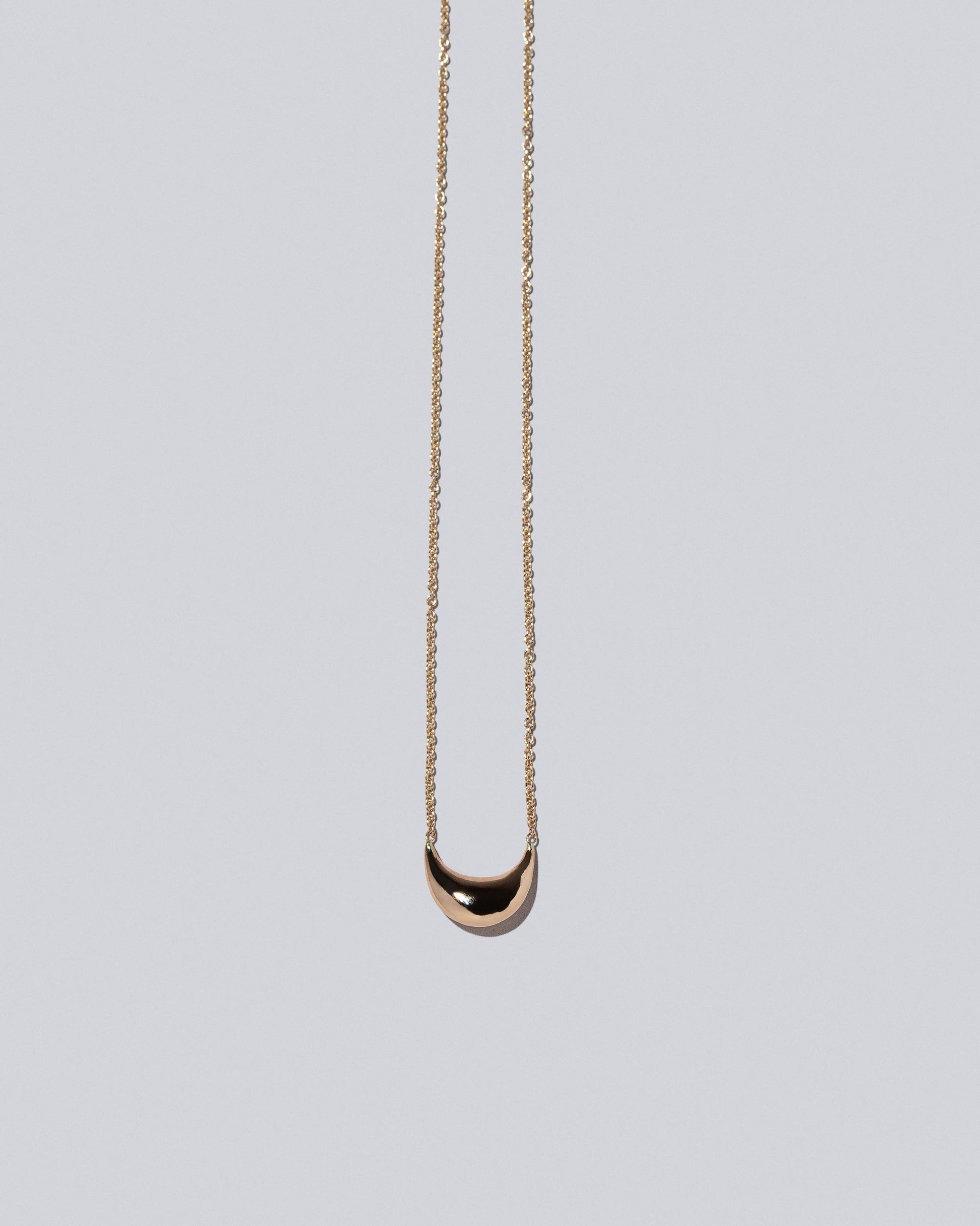 Closeup detail of Half Moon Time Capsule Necklace on light color background.