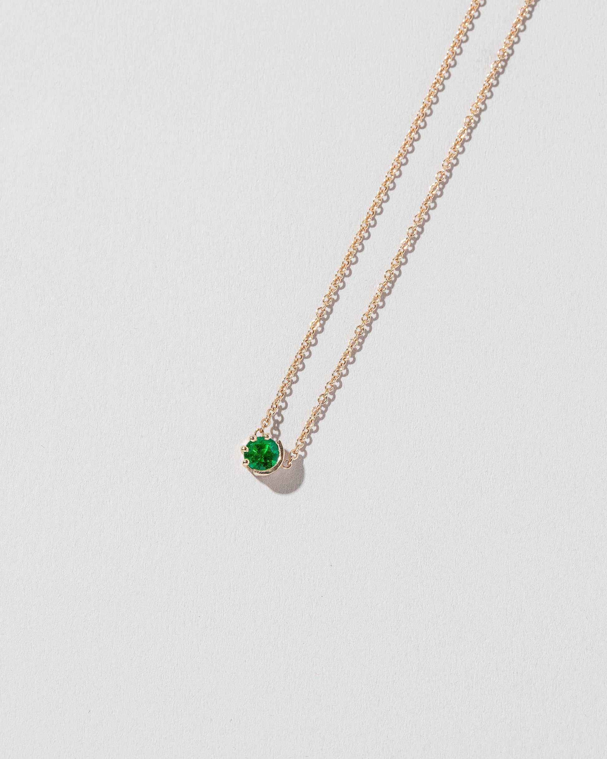 Closeup details of the Emerald Sun & Moon Necklace on light color background.