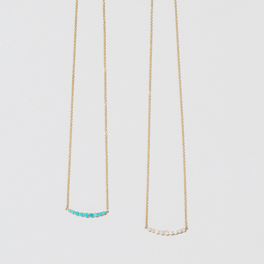 product_details::Closeup detail of the Opal Crescent Necklace and Turquoise Crescent Necklace on light color background.