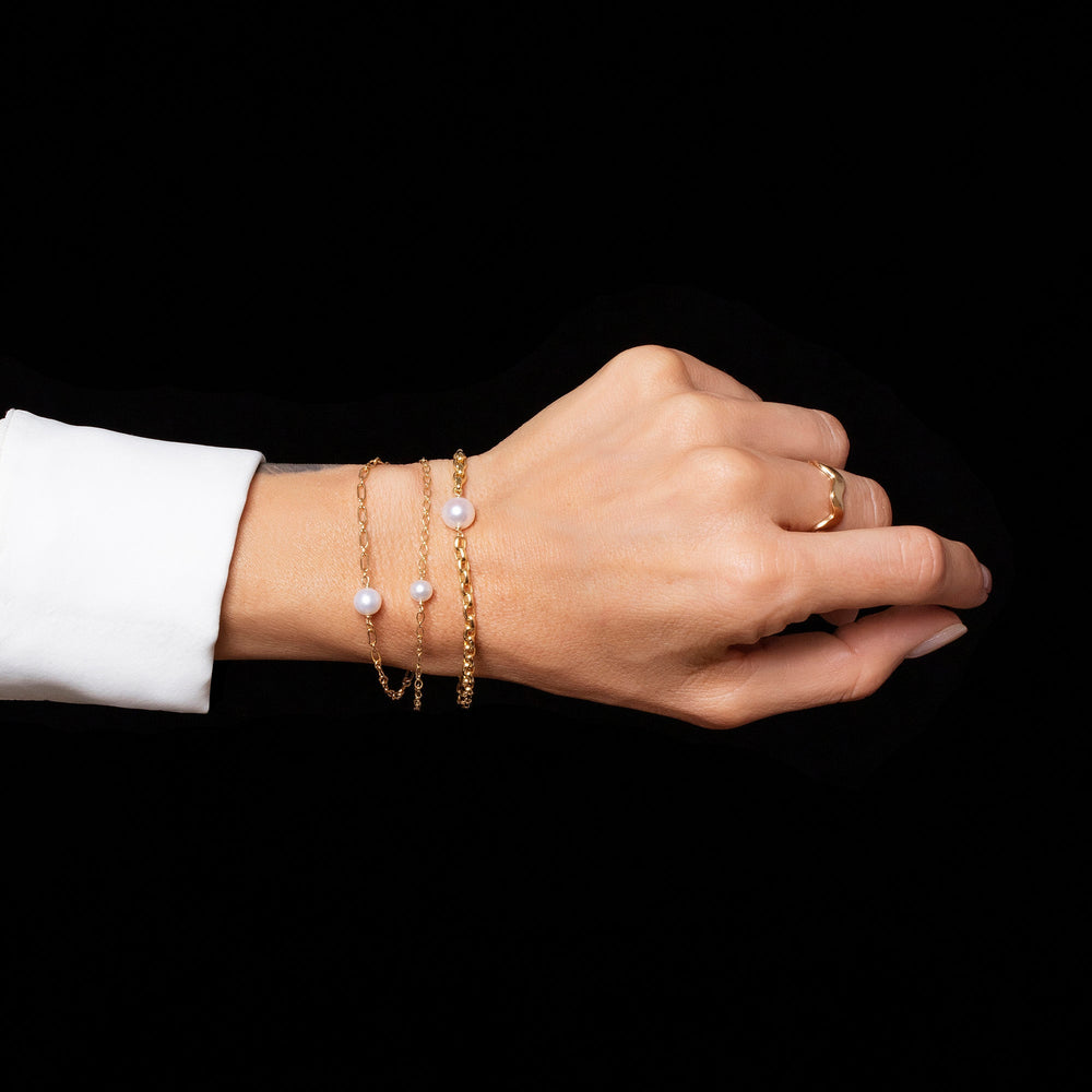 product_details::One Station Bracelet Short Loop Chain, One Pearl Station Bracelet Open Oval Chain, One Pearl Station Bracelet Hot Dog Chain and Gold 5mm Ripple Band on model.