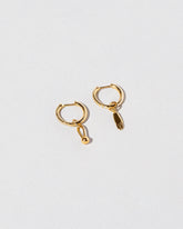 Gold Classic Diamond Snack Hoop Earrings with the Hand Talisman Charm and Loop & Sphere Talisman Charm on light color background.