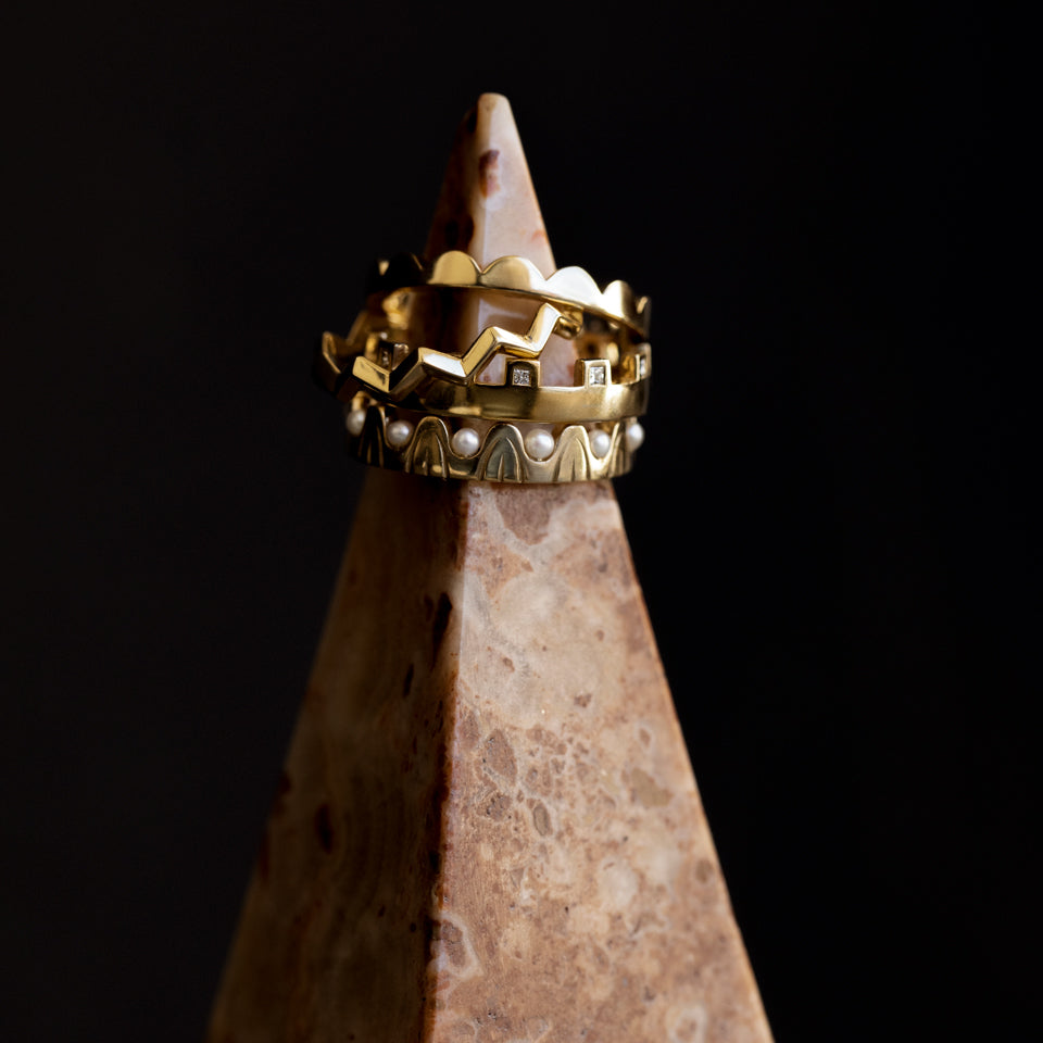 product_details::Eternal Moon Band, Perfect Balance Band, Connection Band with White Diamonds, and Pearls of Wisdom Band on stone pyramid against dark colored background.