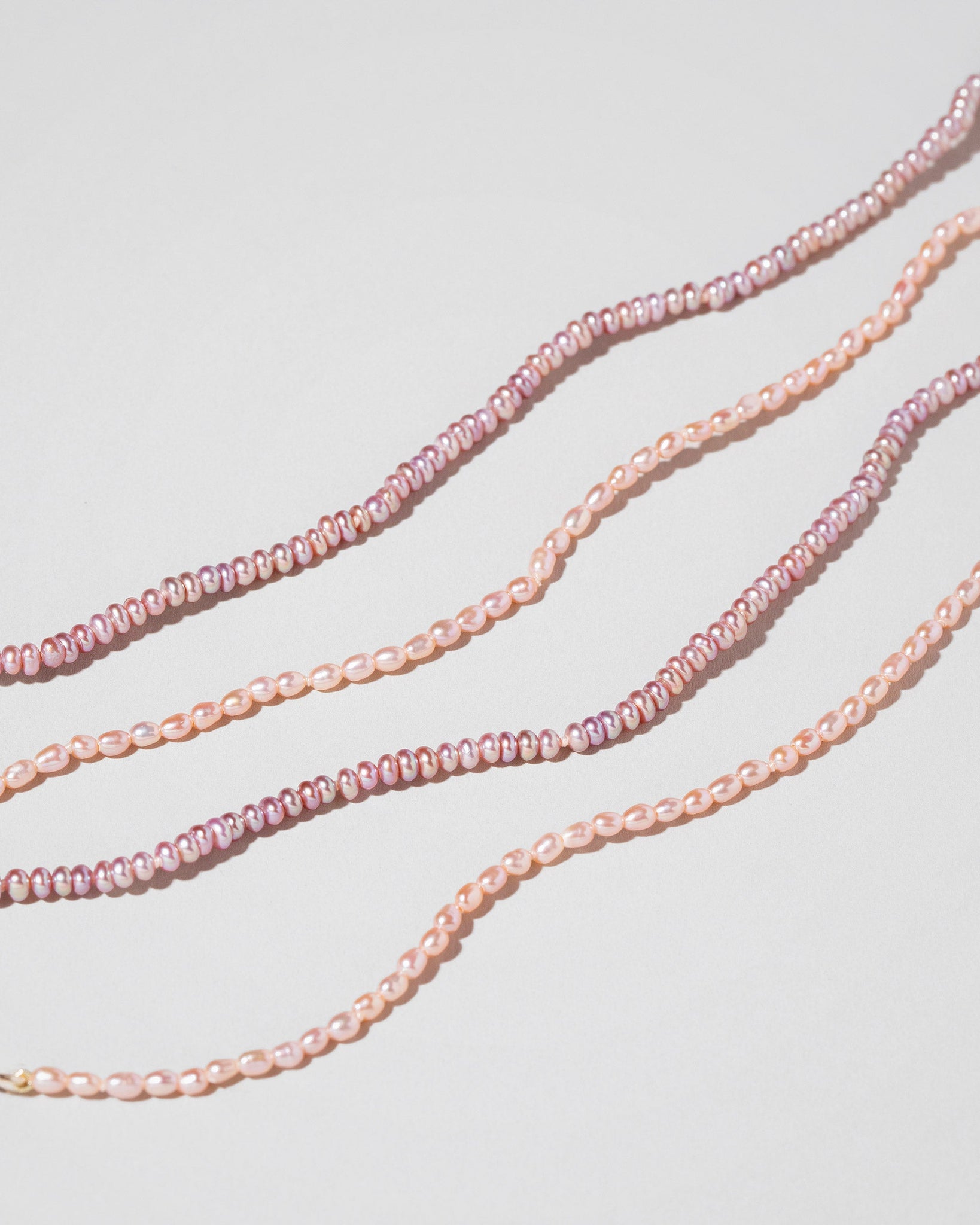 Closeup details of the Pink Lavender Seed Pearl Anklets and Pink Peony Oval Pearl Bracelets on light color background.