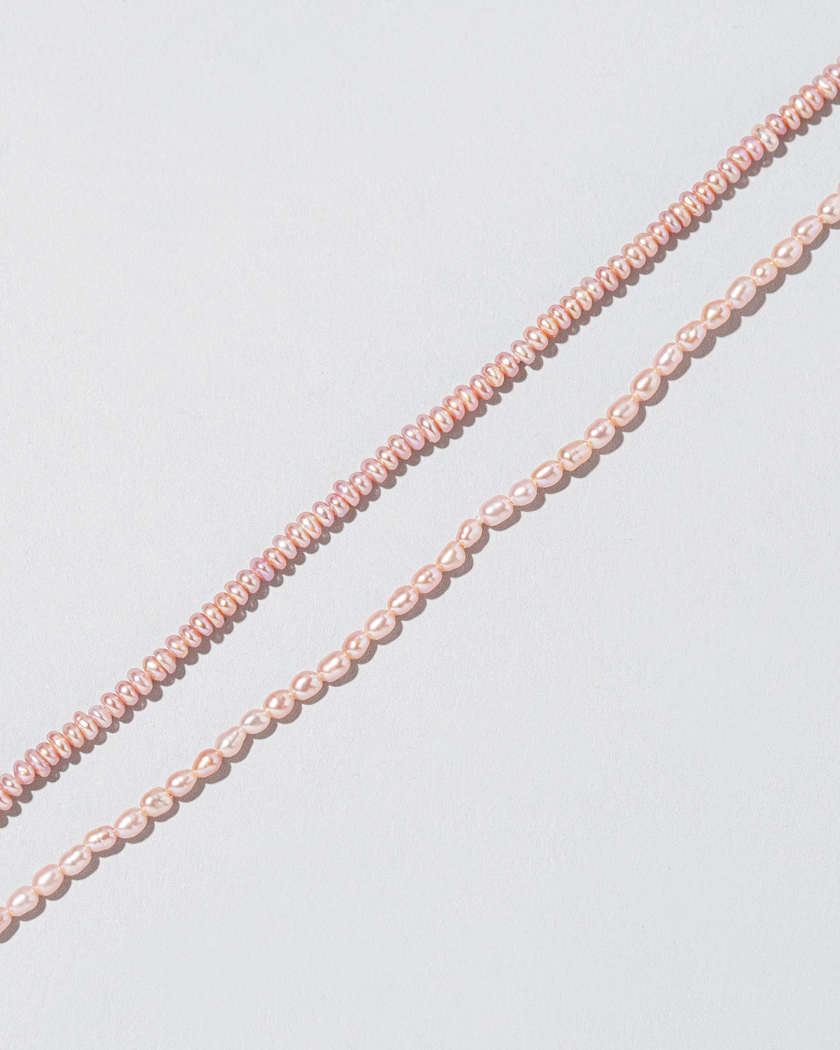 Closeup details of the Pink Peony Seed Pearl Anklet and Pink Peony Oval Pearl Bracelet on light color background.