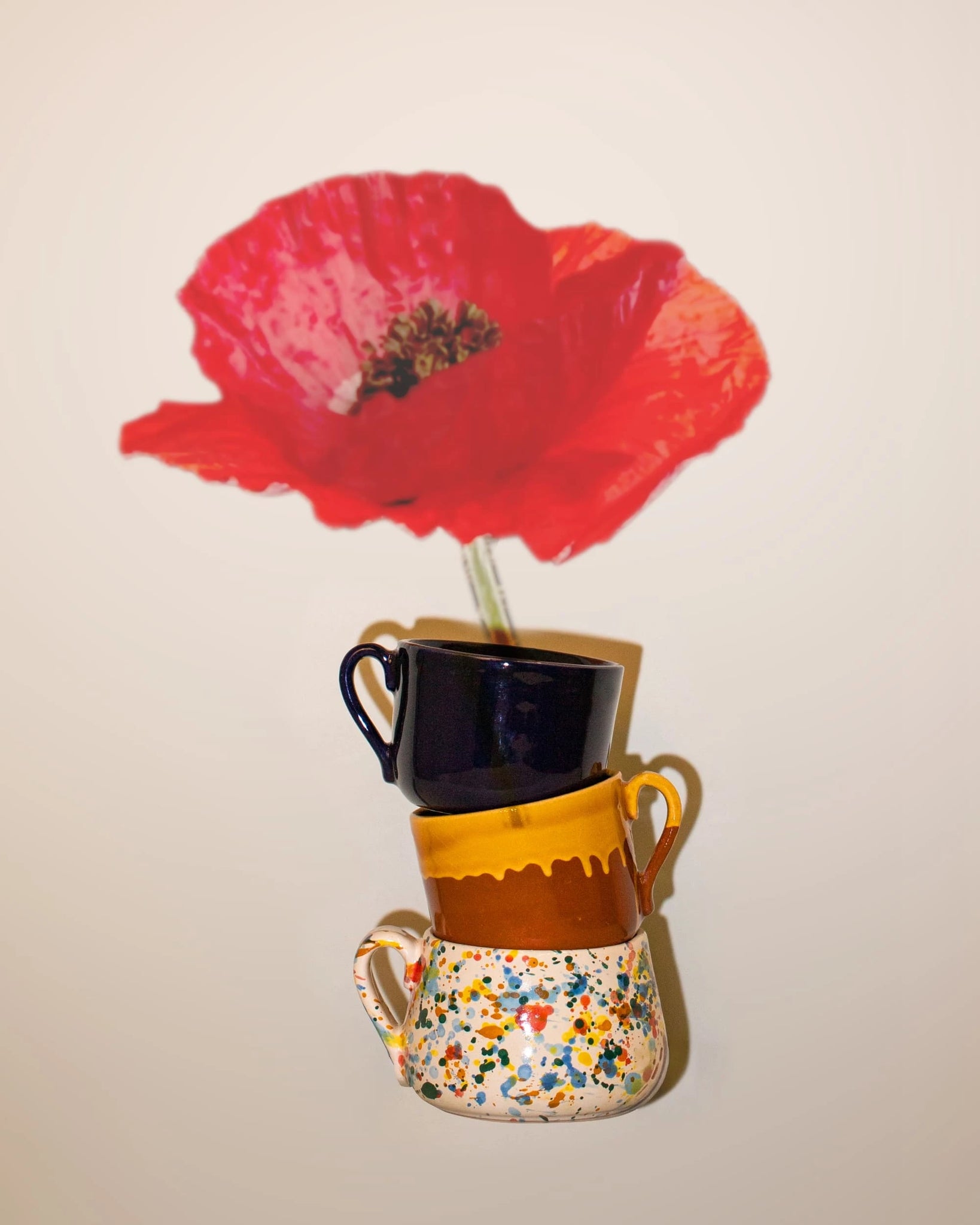 Editorial photo of three La Ceramica Vincenzo Del Monaco mugs with an oversized poppy flower on a tan background