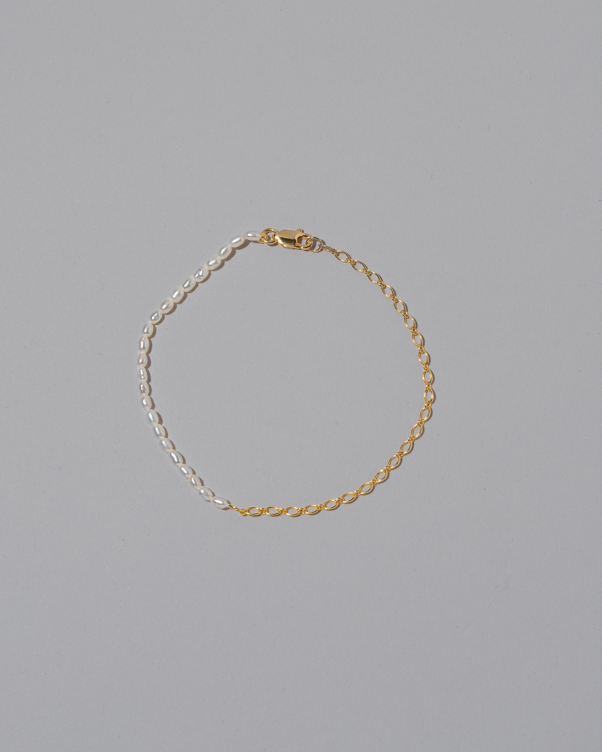 Half Oval Chain & White Seed Pearl Bracelet on light color background.