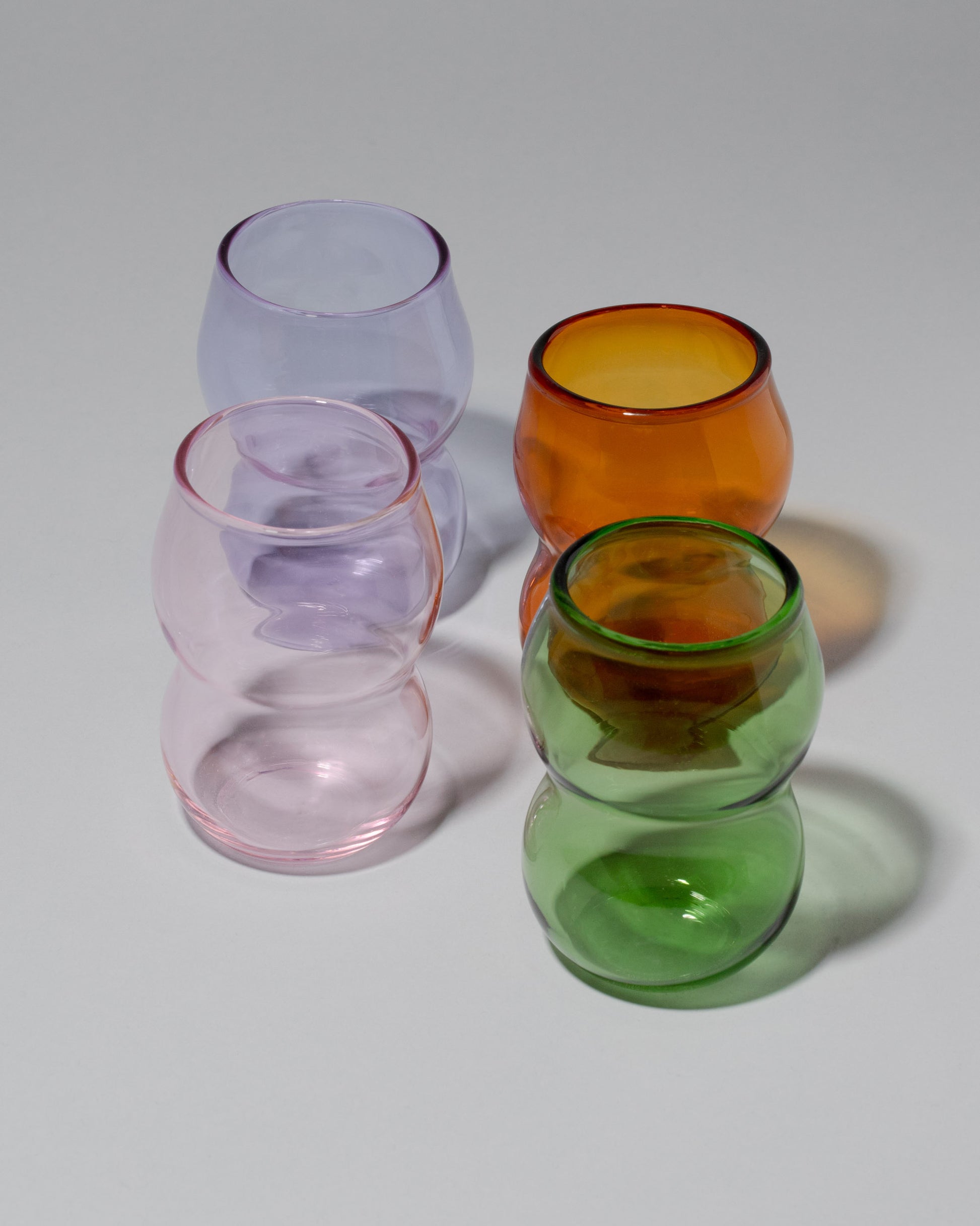 Group of Ornamental by Lameice Green, Lilac, Pink and Amber Transparent Dreamlike Cups on light color background.