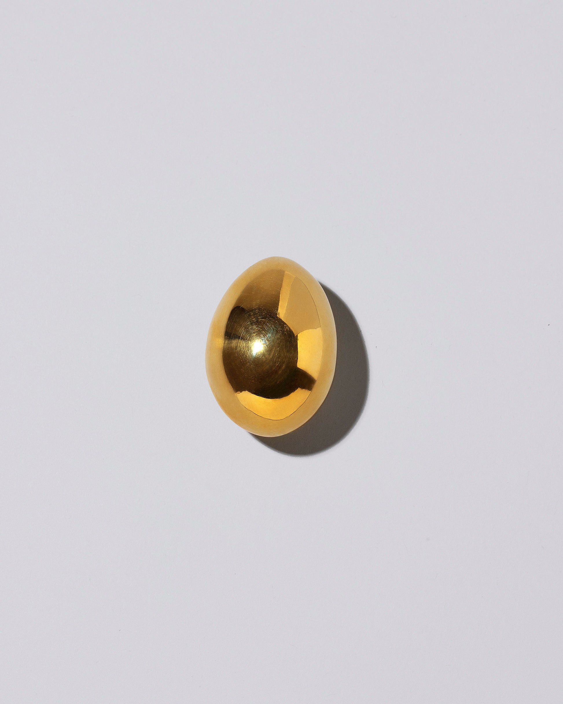 Carl Auböck Brass Egg Paperweight on light color background.