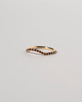 View from the side of the Gold Garnet Pavé Mini Curve Band on light color background.