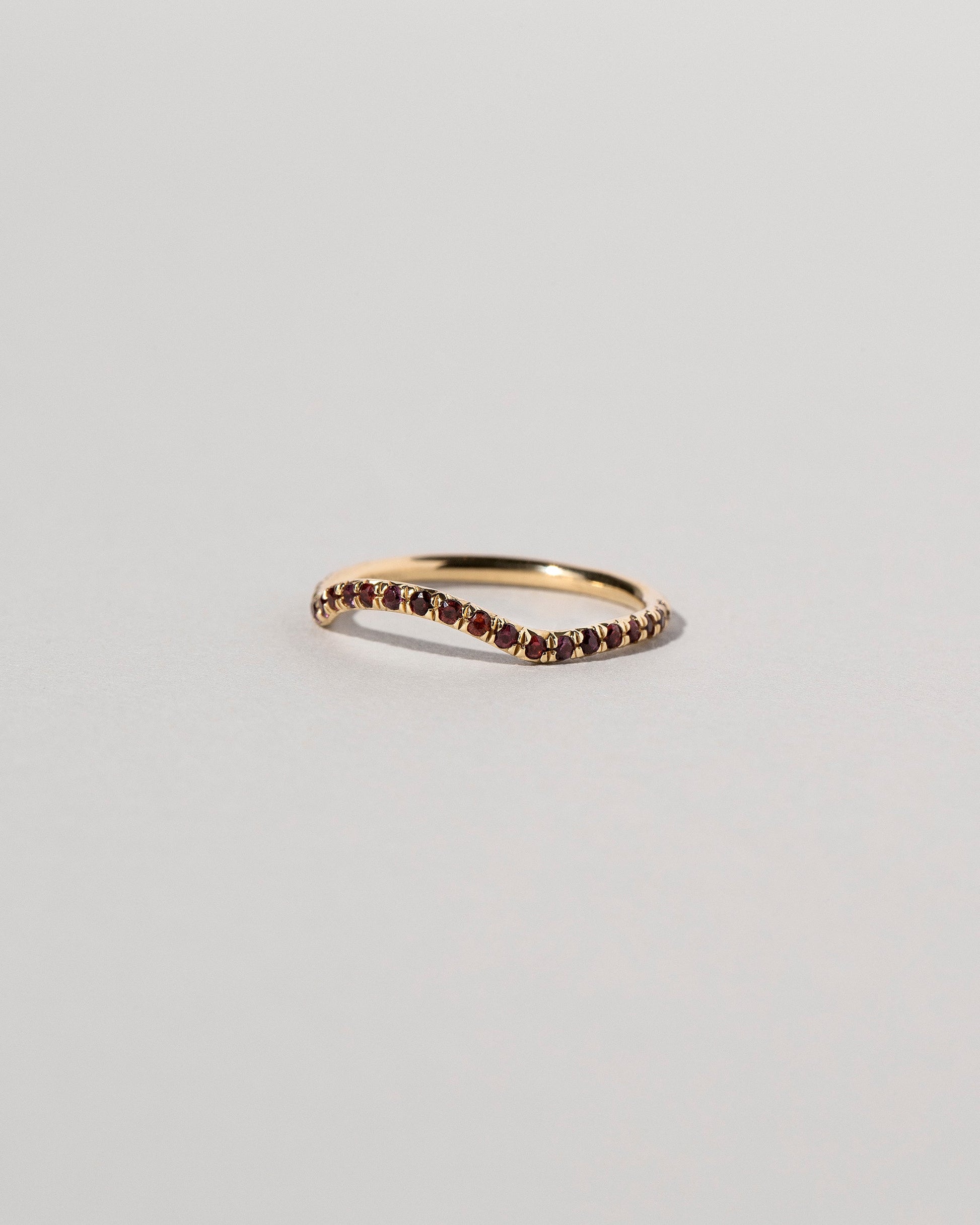 View from the side of the Gold Garnet Pavé Mini Curve Band on light color background.