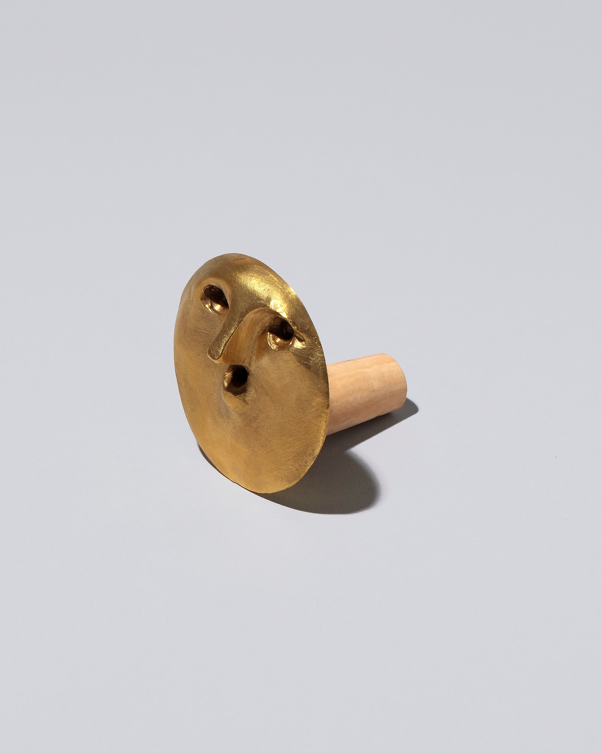 View from the side of the Carl Auböck Uranio Brass Face Bottle Stopper on light color background.