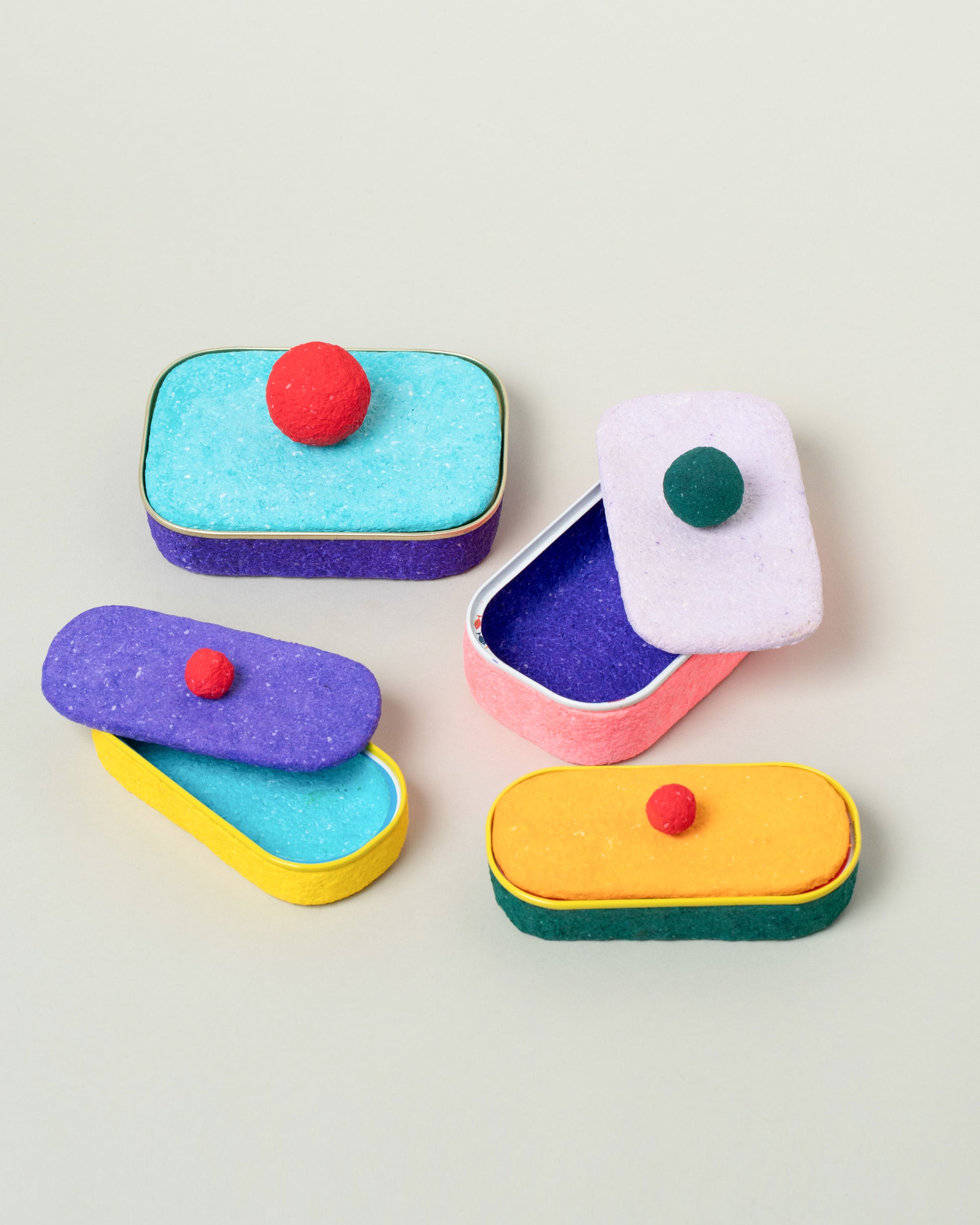 Chiaozza Turquoise For Your Pleasure Large Sardine Can, Lilac For Your Pleasure Medium Sardine Can and Purple and Mustard For Your Small For Your Pleasure Sardine Cans on light color background.