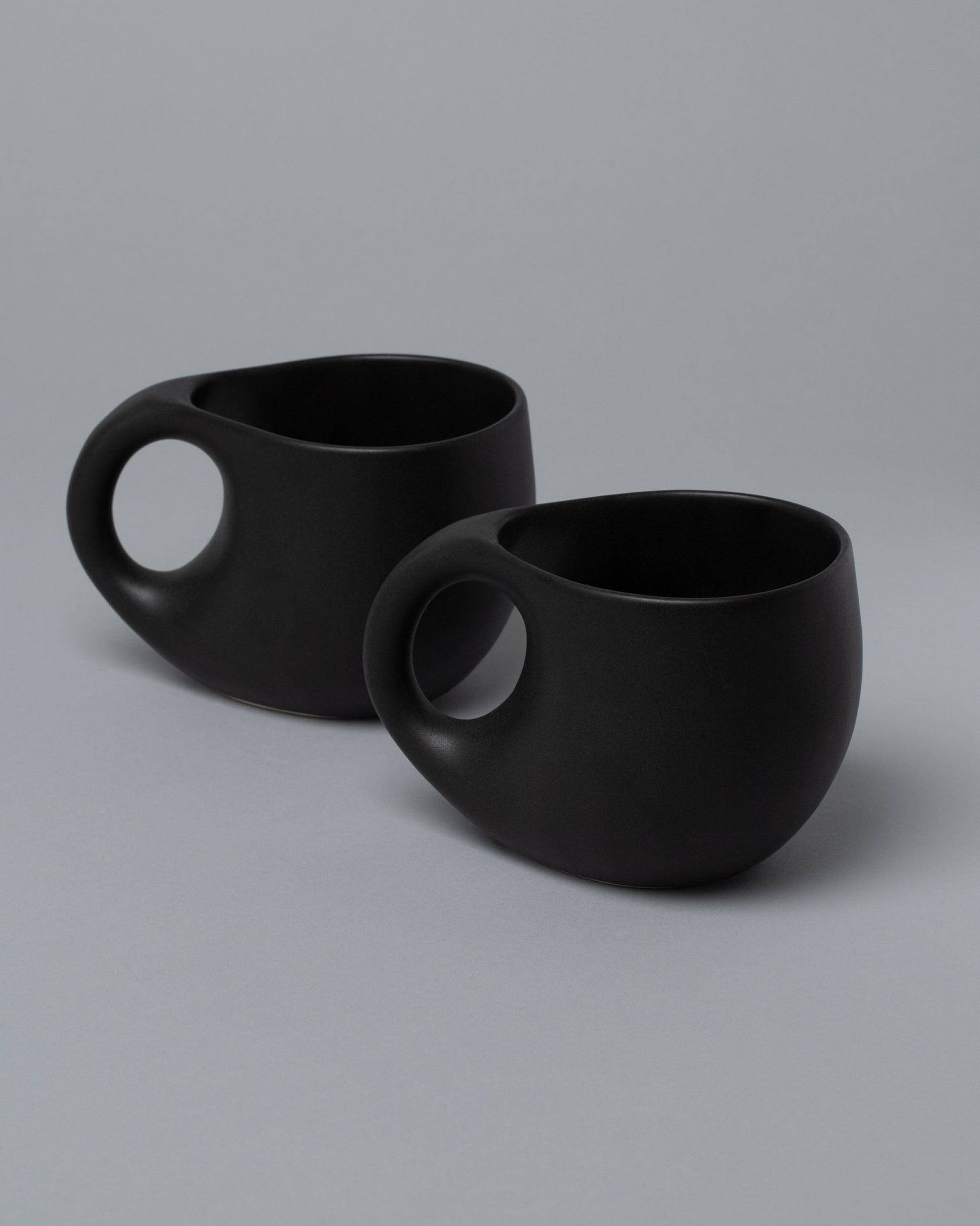Closeup view of half of the Dust and Form Mugs Set, including the Large Charcoal Comfort Mugs on light color background.