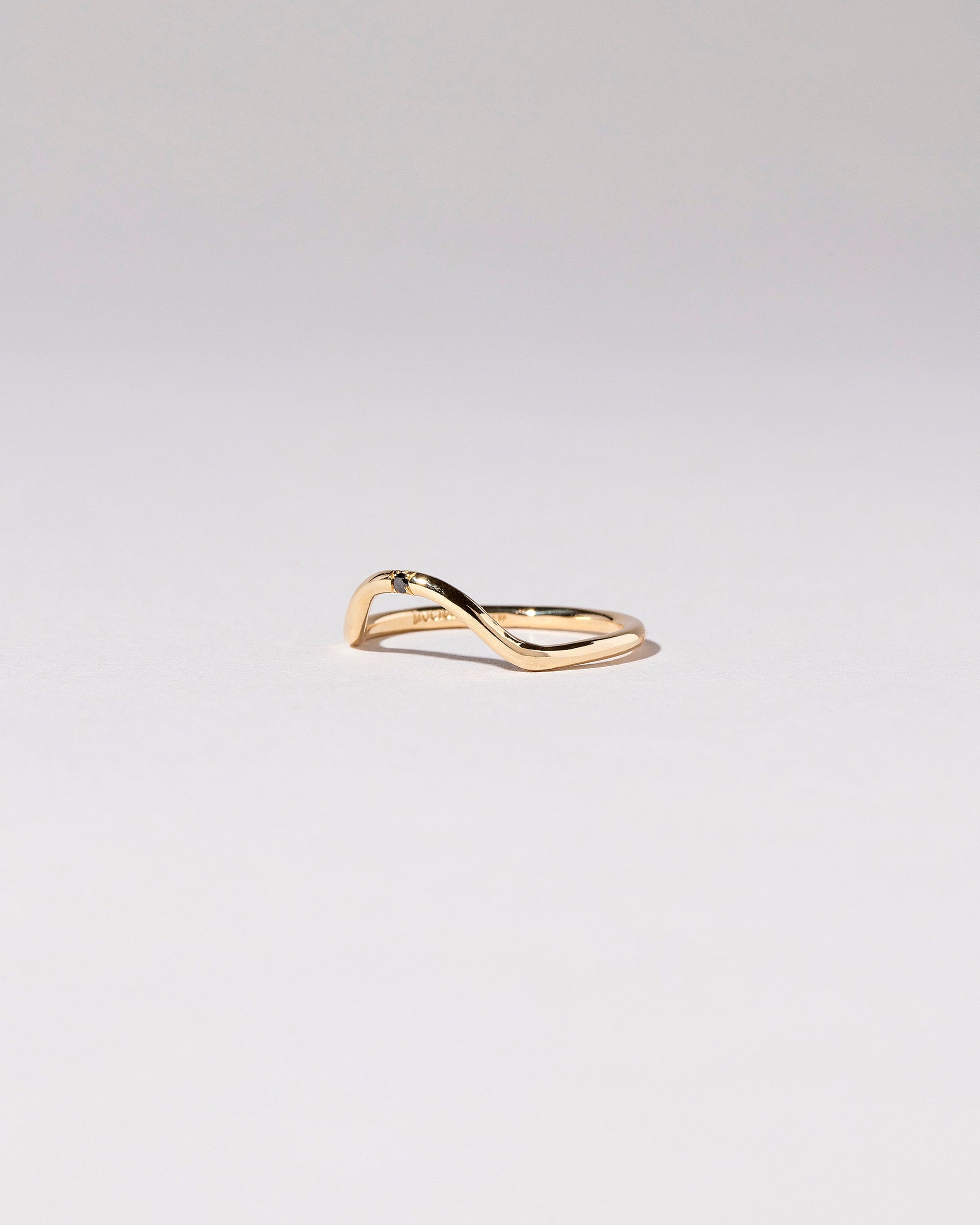 View from the side of the Gold Single Stone Black Diamond Curve Band on light color background.