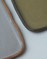 Closeup details of the Emris Brick Clay Scalloped Tray and Dark Stoneware Scalloped Tray on light color background.