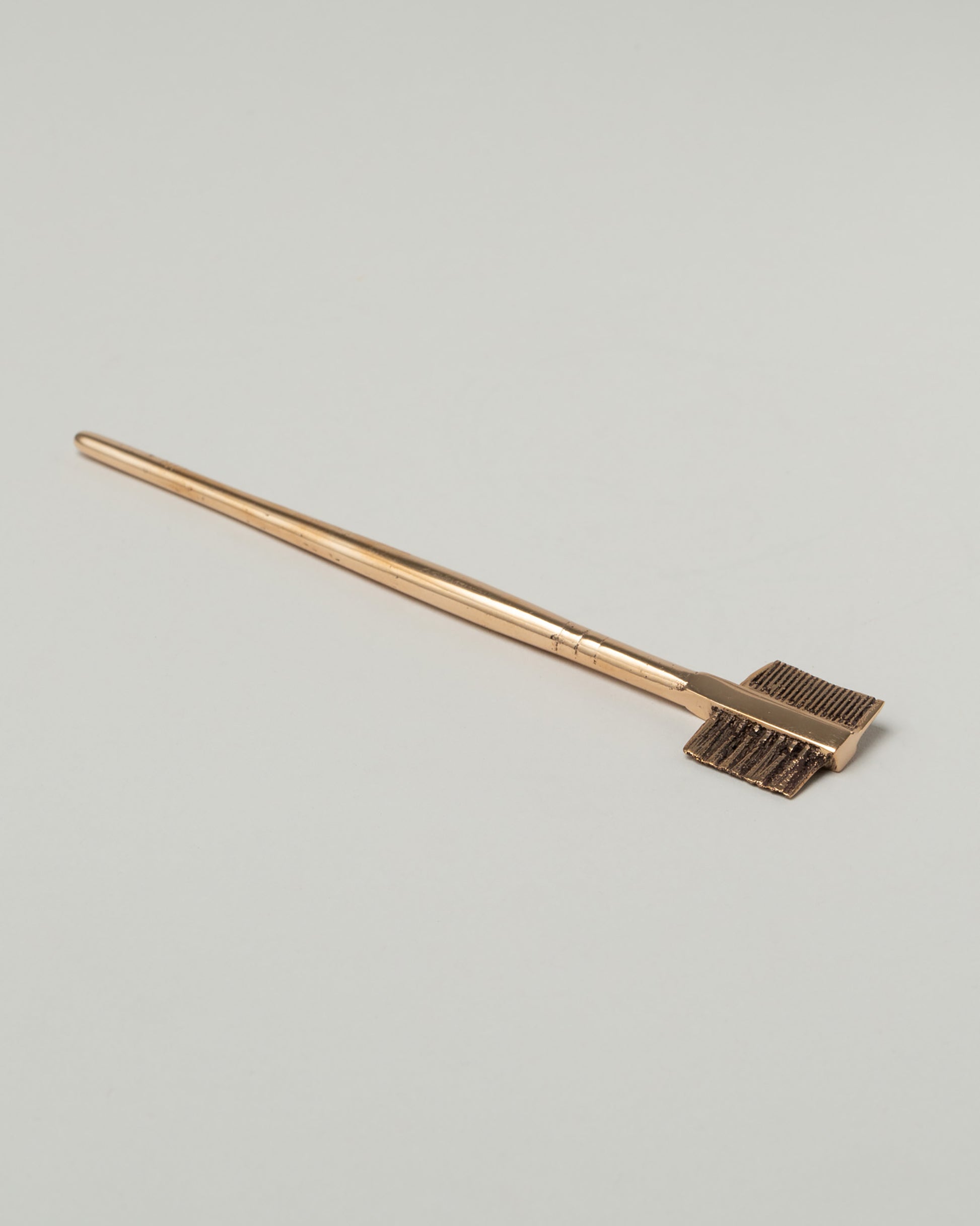 Pearce Objects Cast Brass Eyebrow Brush on light color background.