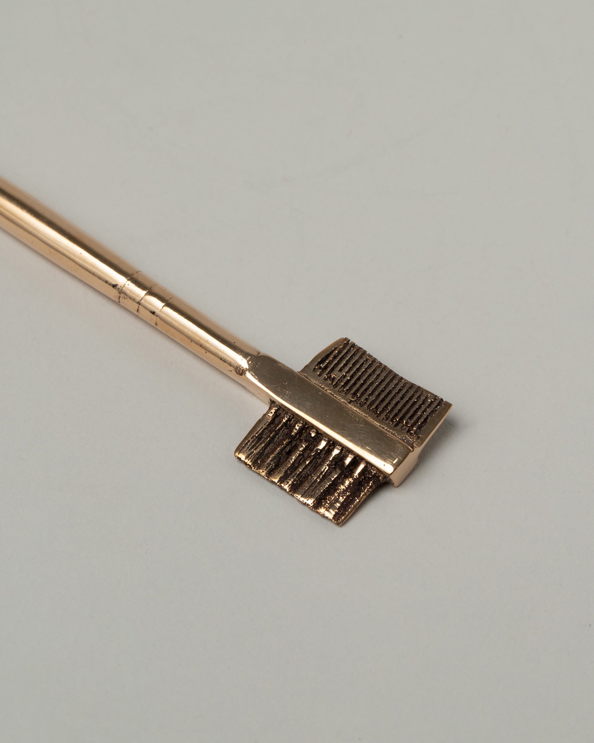 Closeup details of the Pearce Objects Cast Brass Eyebrow Brush on light color background.