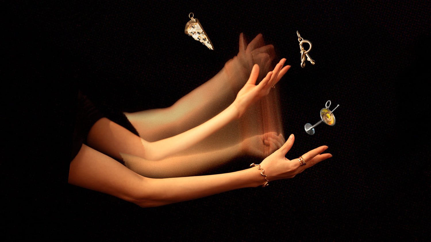 Styled long exposure image featuring the Veggie Slice Pizza Charm, Dirty Martini Charm, Gold Cut-Outs Bracelet and CRZM by Mociun Gold R Letter Charm on dark color background.