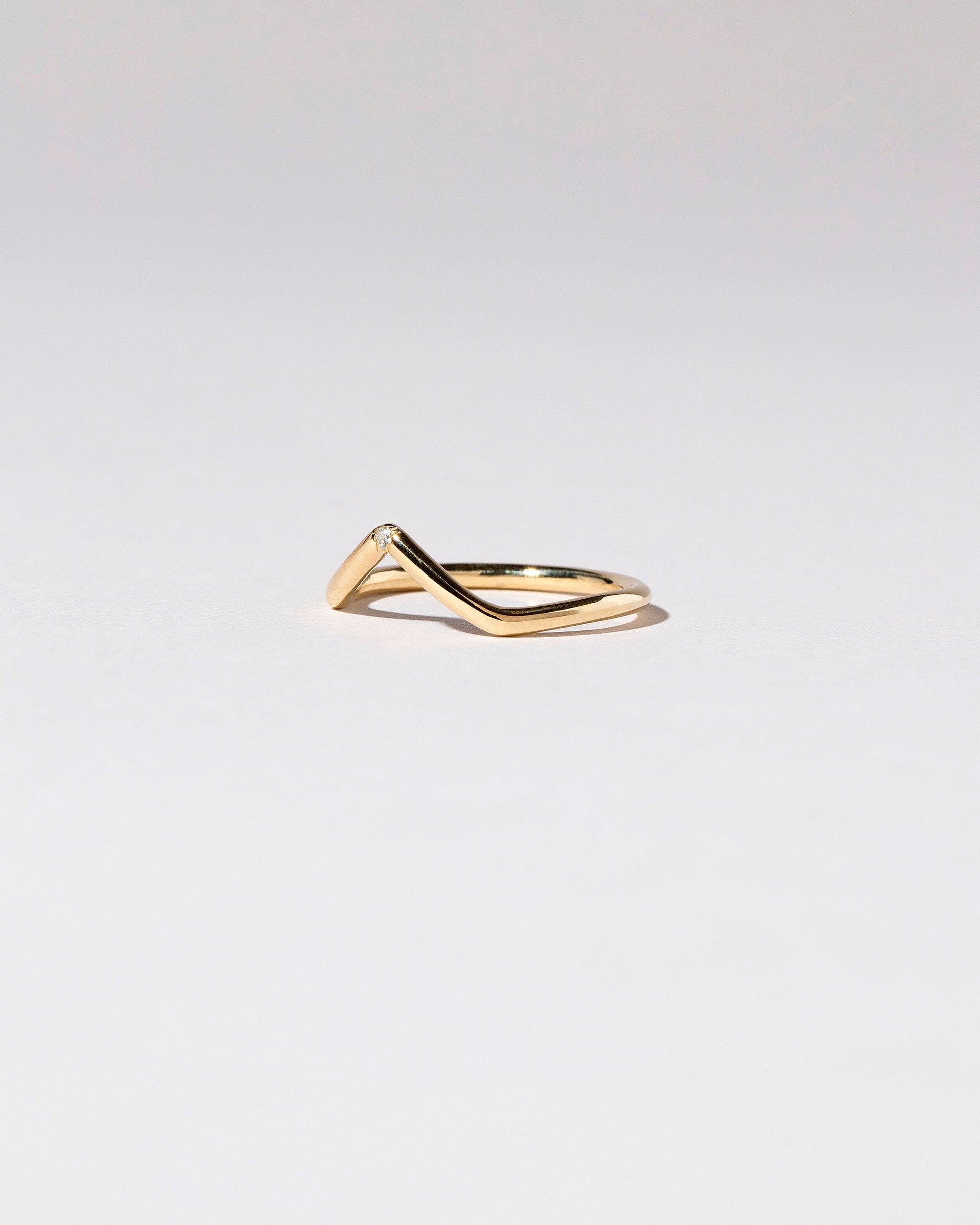 View from the side of the Gold Single Stone White Diamond High Peak Band on light color background.