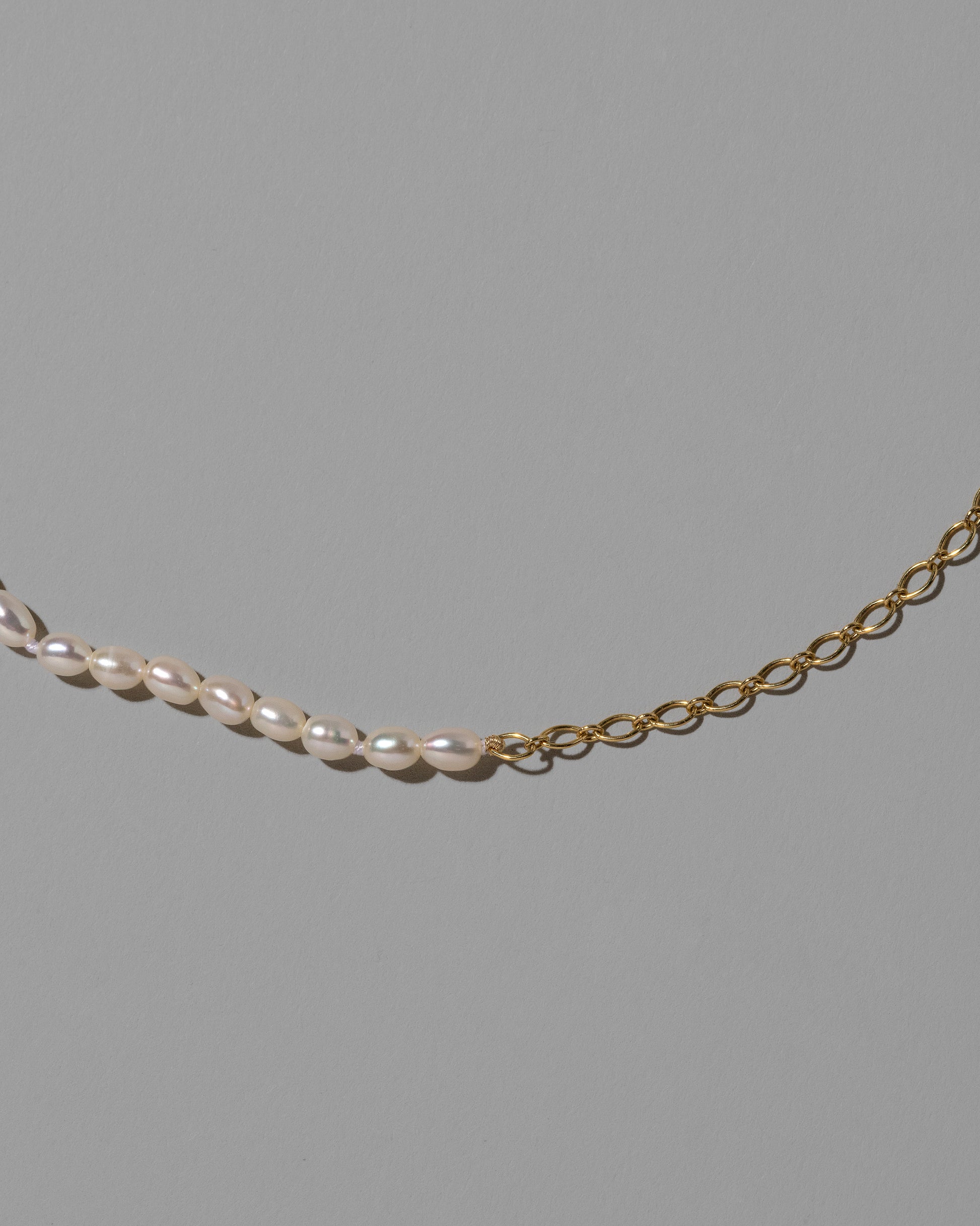 Closeup details of the Half Oval Chain & White Seed Pearl Necklace on light color background.